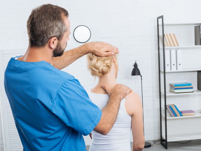 chiropractor stretching neck of woman during appointment in hosp