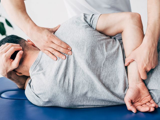 Back view of chiropractor massaging back of man lying on Massage